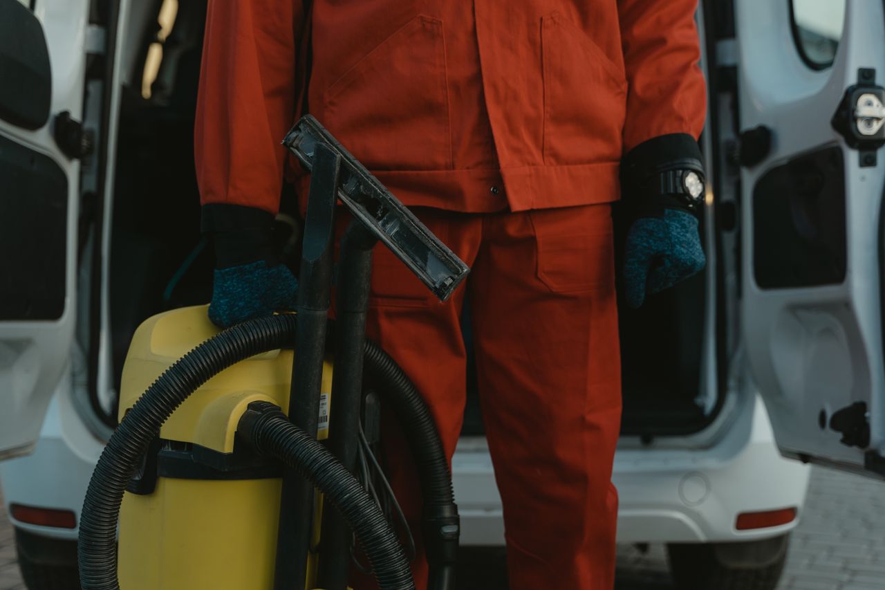 gallery-01 A professional cleaner in a red uniform holding a vacuum near a van, ready for service.