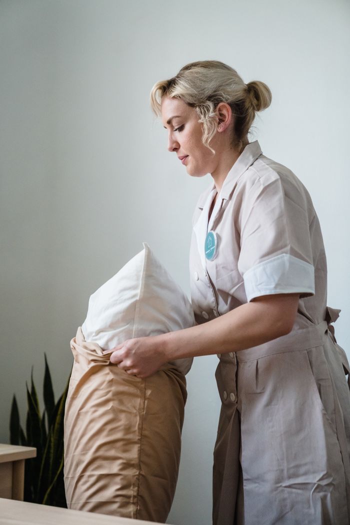 gallery-05 Hotel maid in uniform arranging pillows in a neatly styled guest room.